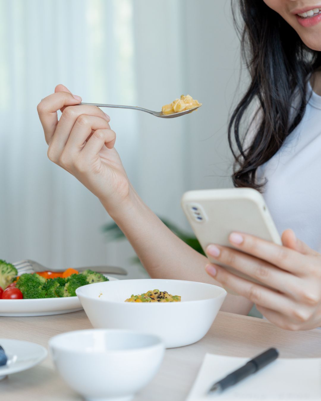 Mujer comiendo una ensalada mientras consulta el móvil