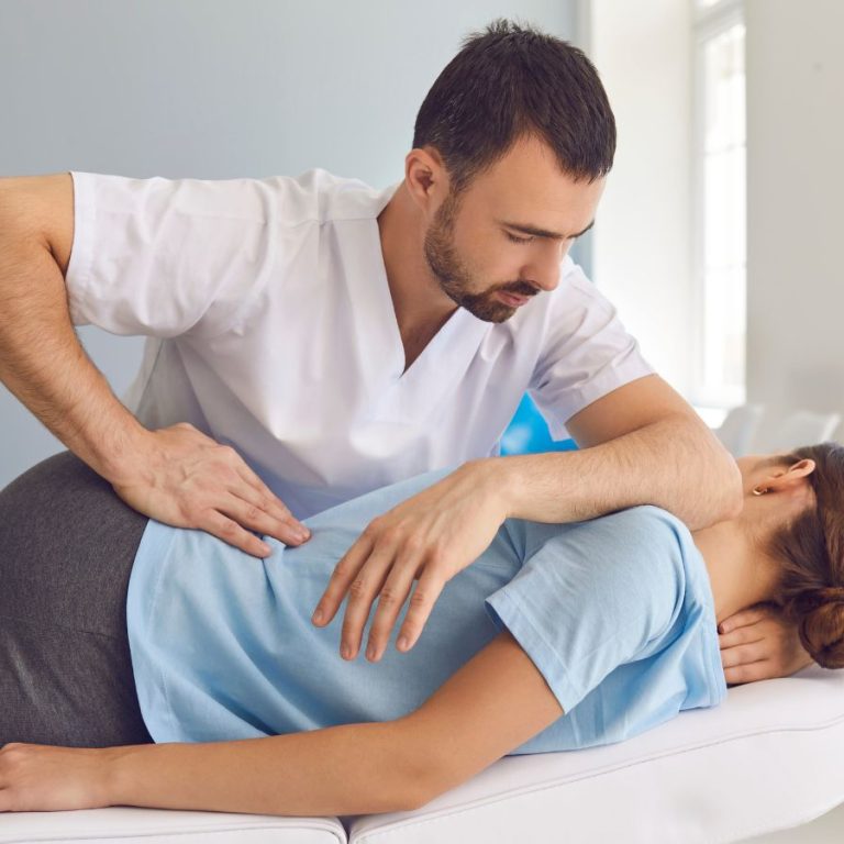 Fisioterapeuta aplicando terapia manual en la espalda de una paciente tumbada en camilla