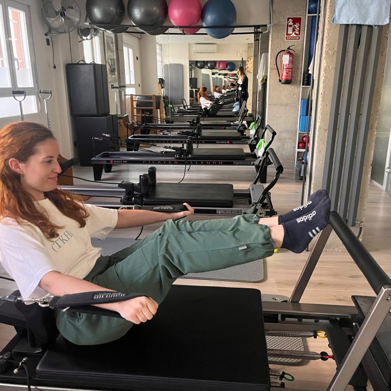 Paciente ejercitándose en una máquina reformer durante una clase de pilates en The Kine Hub